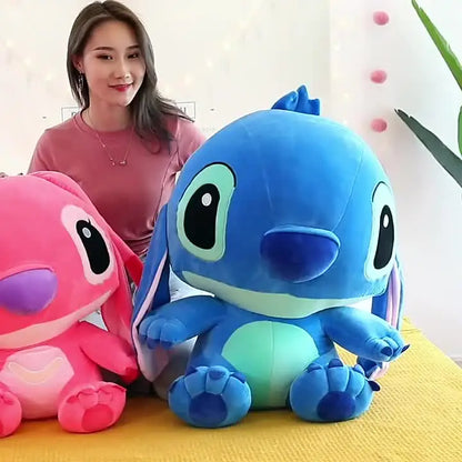 Plavi plišani Stitch izbliza na žutom kauču, rozi lik u pozadini
