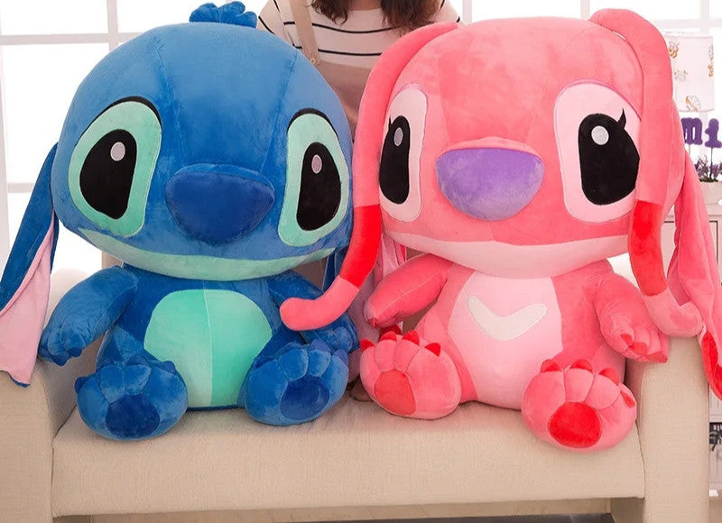 Plavi i rozi plišani Stitch jedan pored drugog na bijeloj sofi